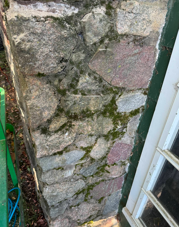 Stone pillar with green moss growing on it, next to a white window frame.