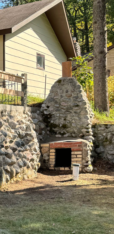 Stone outdoor oven with brick hearth, near a cabin.