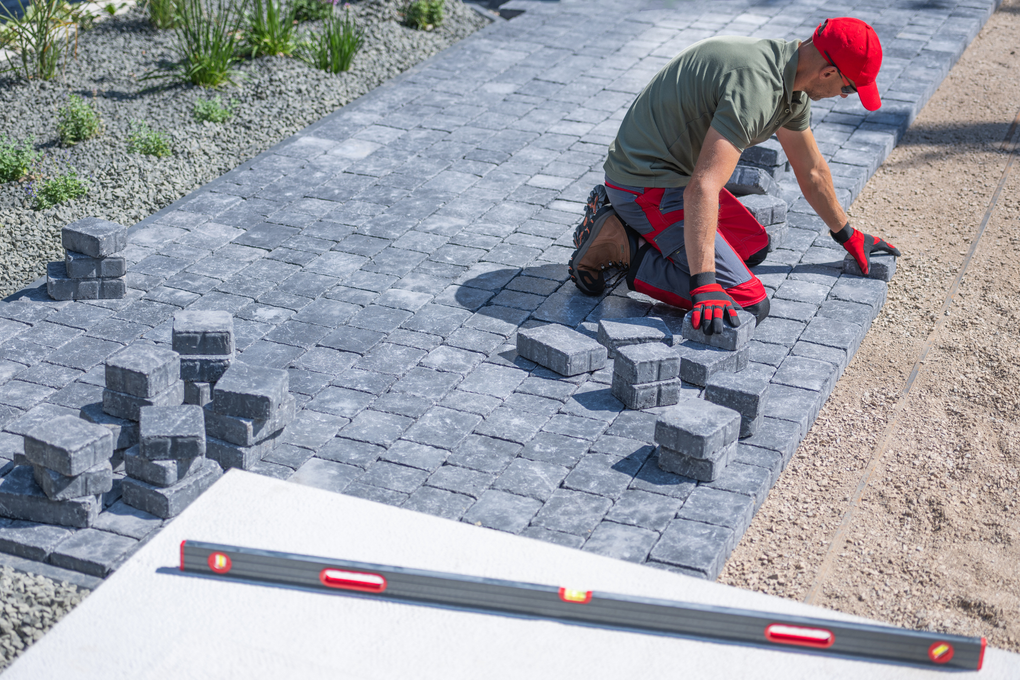 A man is laying bricks on a sidewalk next to a level.