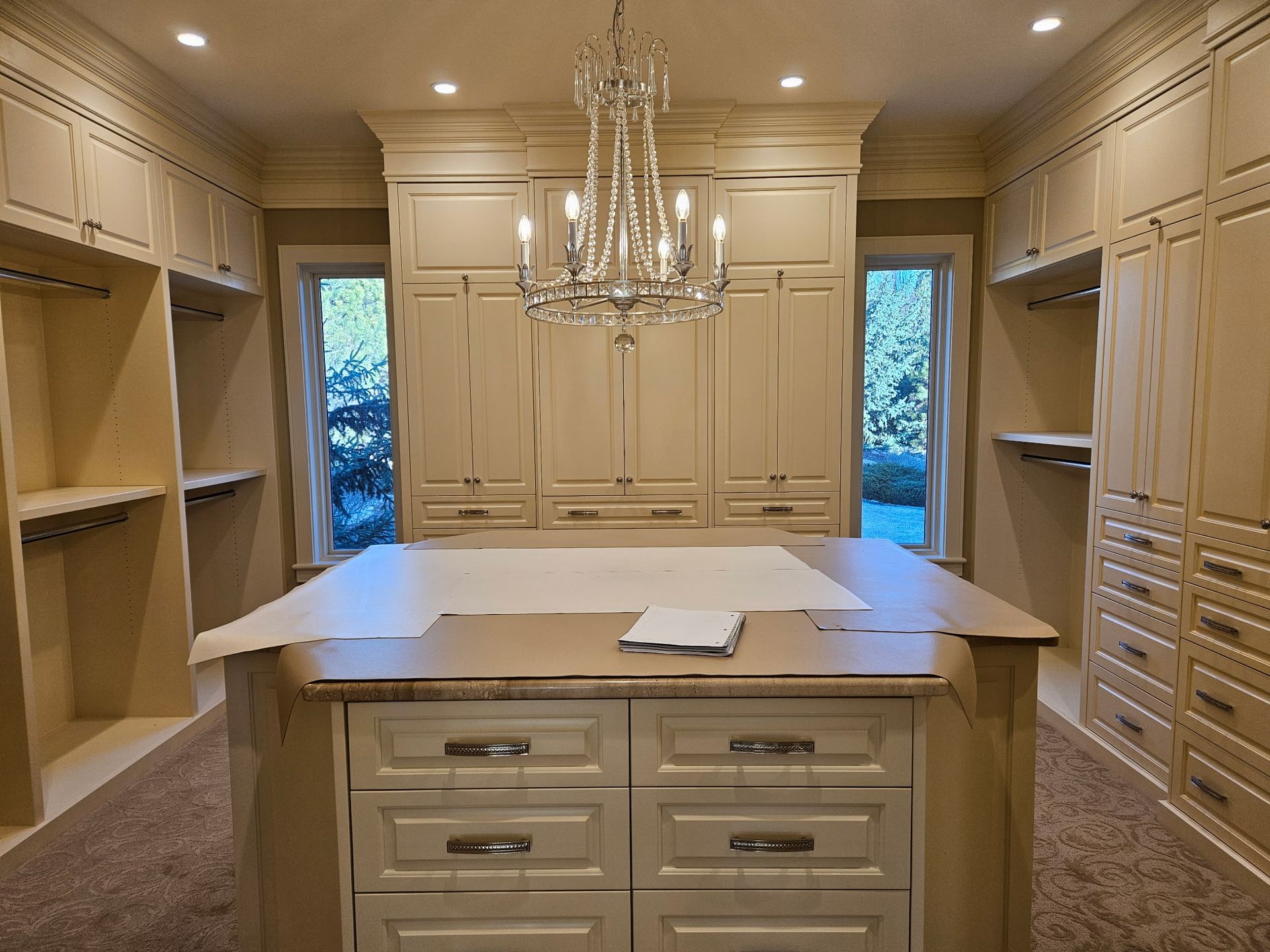 A large walk in closet with lots of cabinets and drawers and a chandelier.