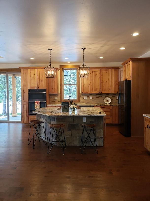 A kitchen with wooden cabinets , granite counter tops , stools and a large island.