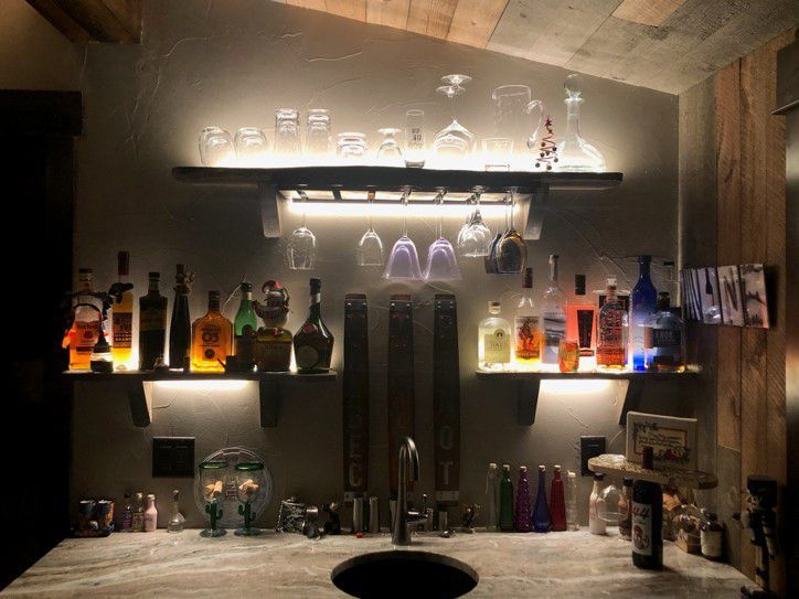 A bar with bottles and glasses on shelves and a sink.