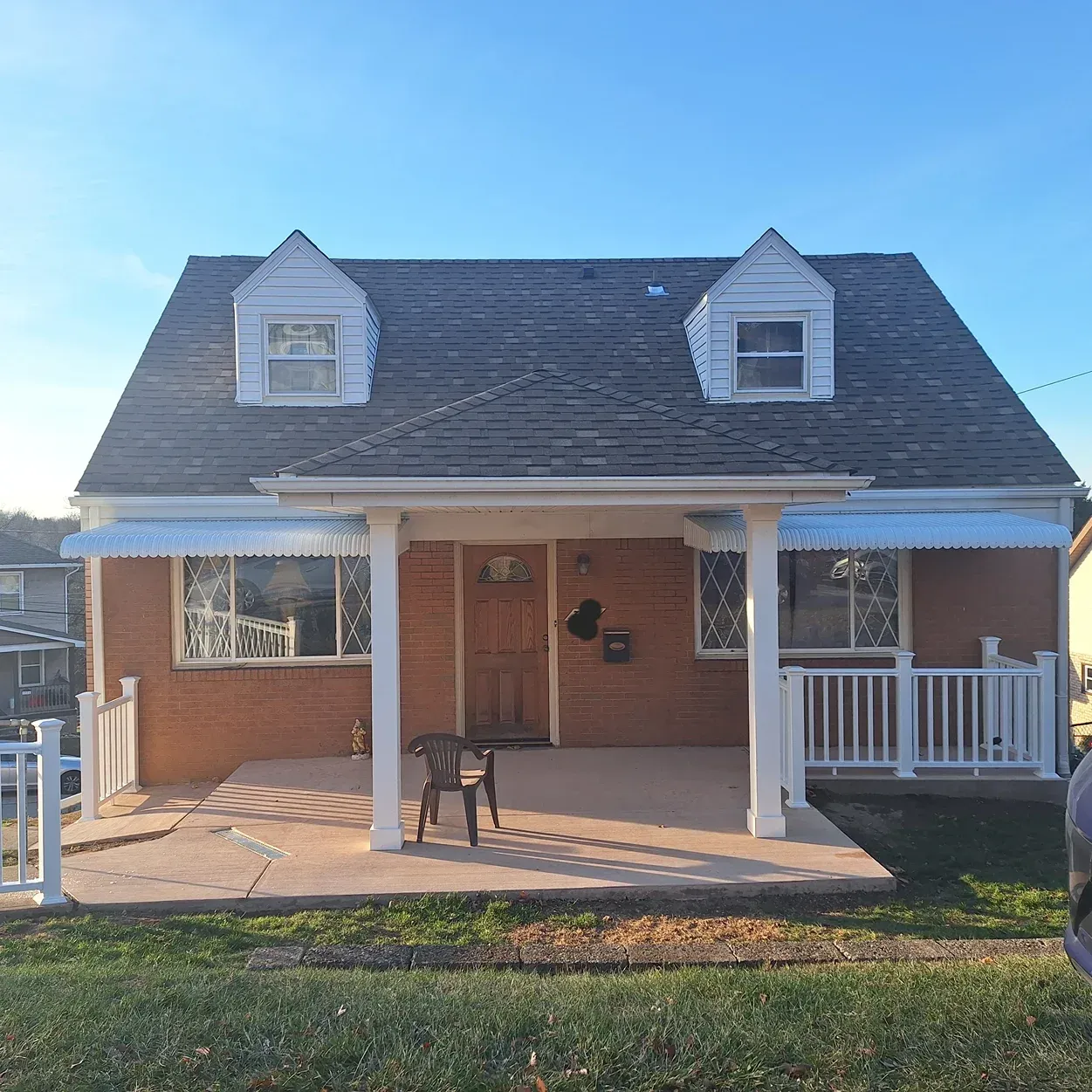 Brick house with porch, two dormers, white trim, and light blue awnings against a blue sky.