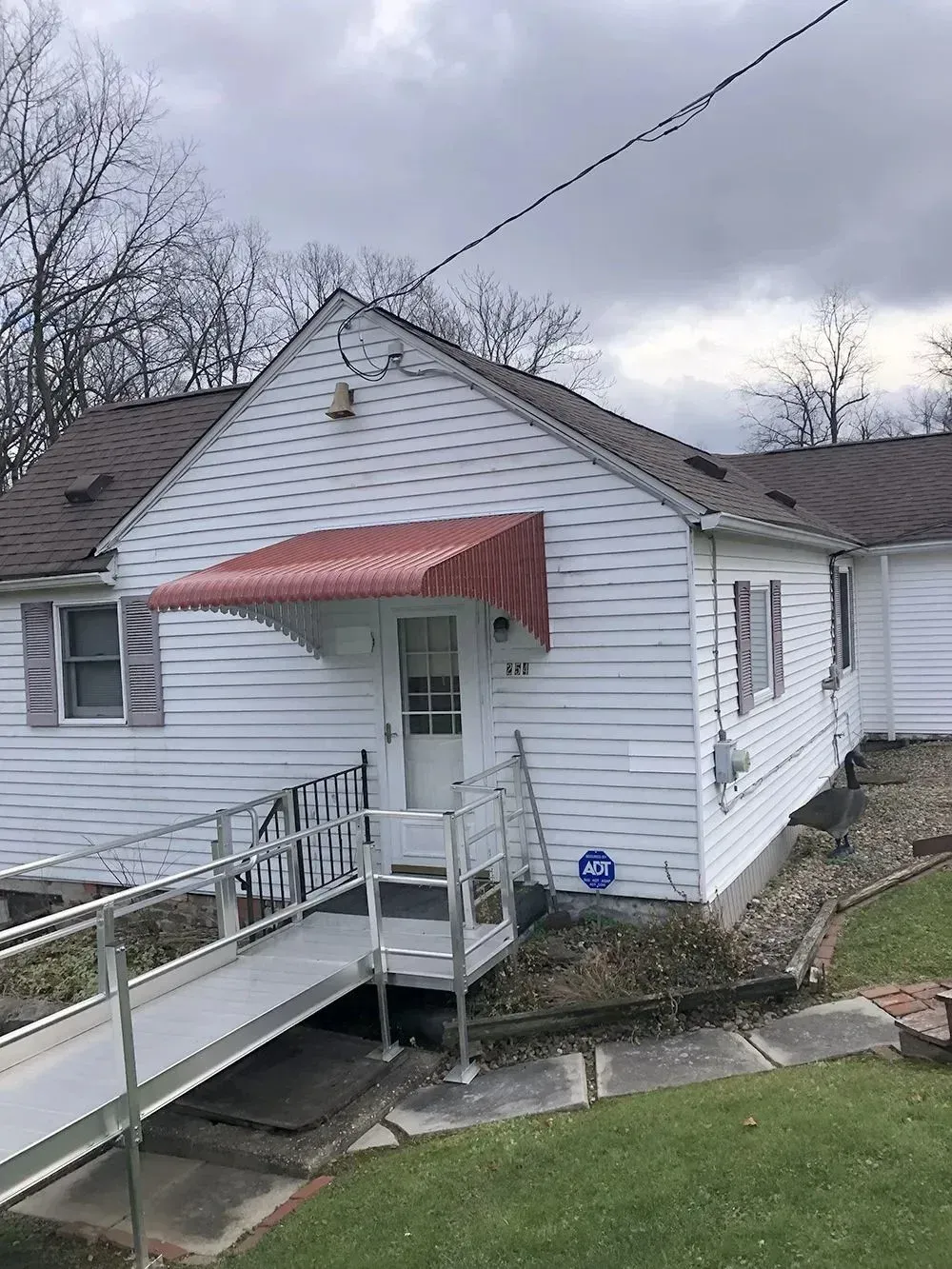 White house with a ramp leading to the front door, red awning over the door.