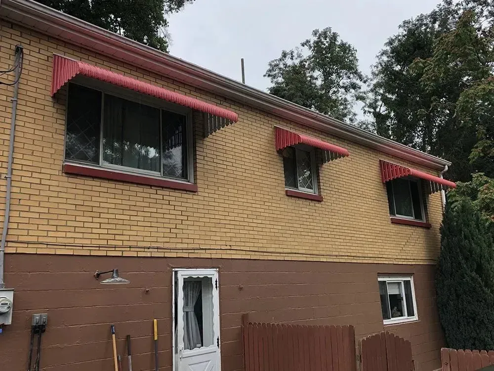 Yellow brick house with red awnings over windows, brown siding below.