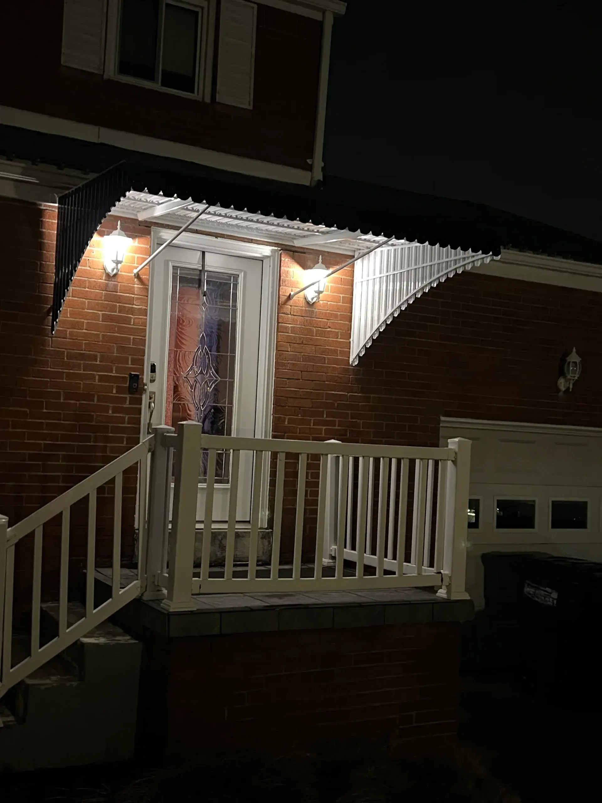 Red brick house at night with white porch and front door, illuminated by lights.