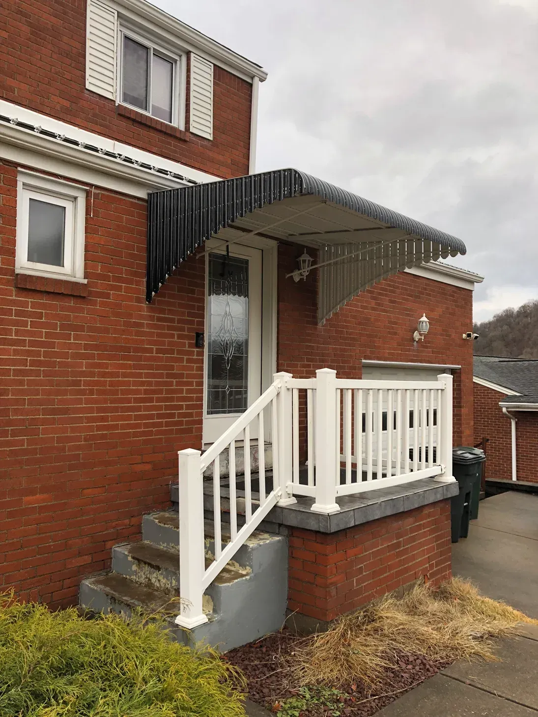 Red brick house with white railing and steps leading to front door under a black awning.