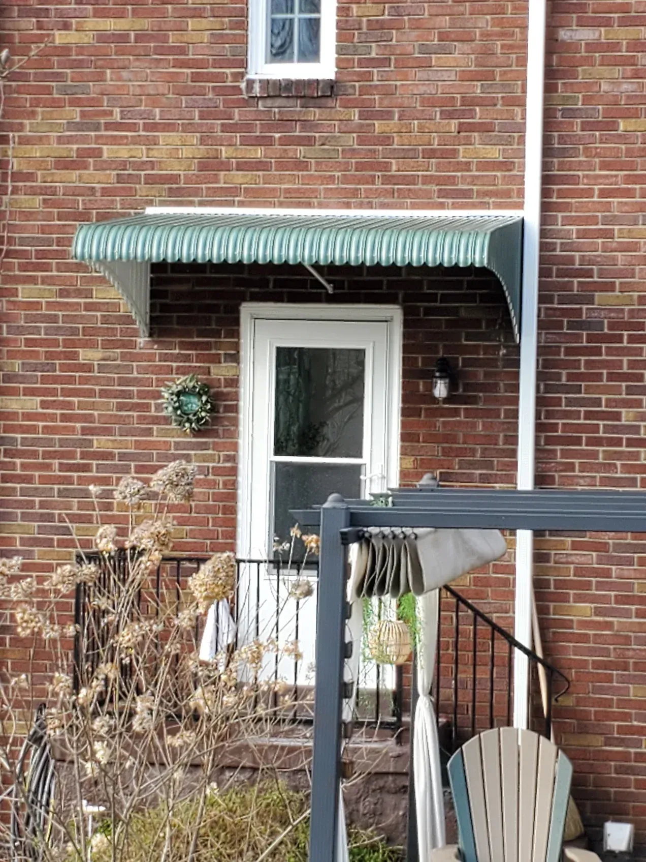 Green and white striped awning over a white door on a brick building with a small window above.