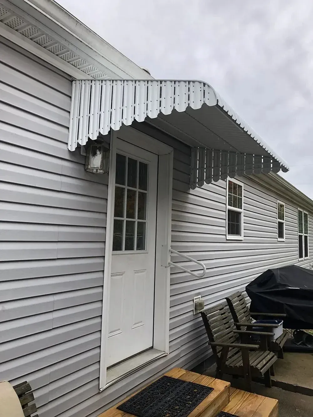 White door with awning, attached to a gray vinyl-sided house.