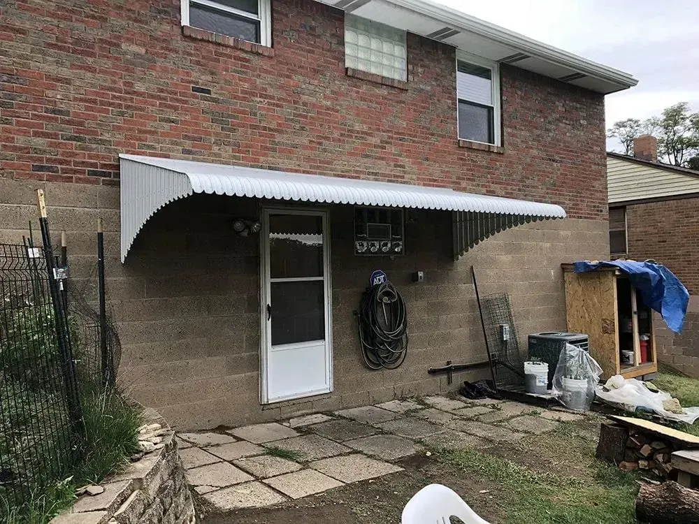 A brick building with an awning over a door, with items like a hose and firewood below.