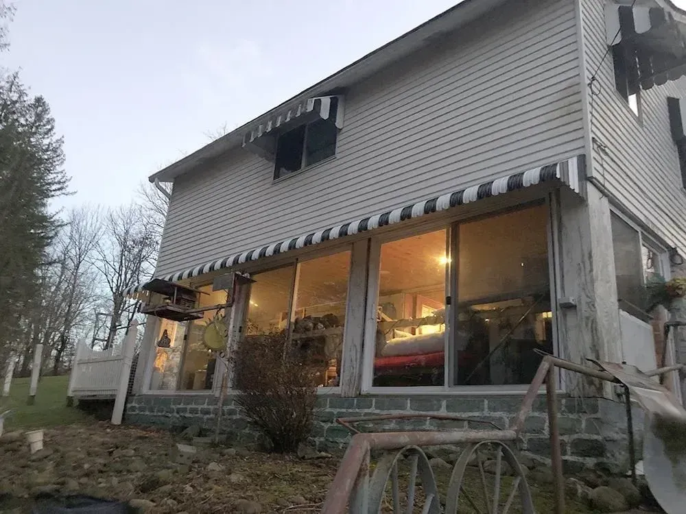 Two-story weathered building with large windows and awnings. Interior light reflects, bird feeder attached.