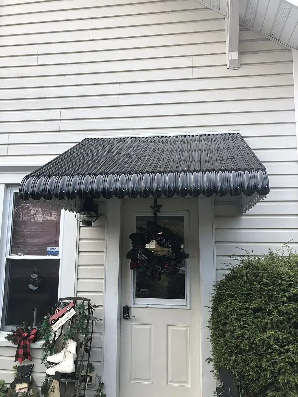 Front door with black awning and a wreath, white siding.