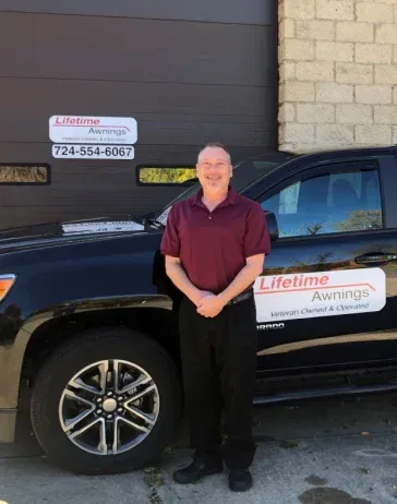 Man in maroon shirt stands next to a black truck with 