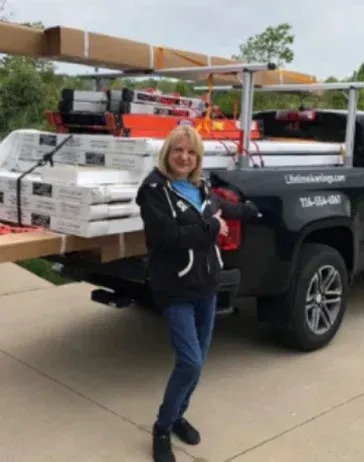 Woman standing by a black pickup truck loaded with construction materials.