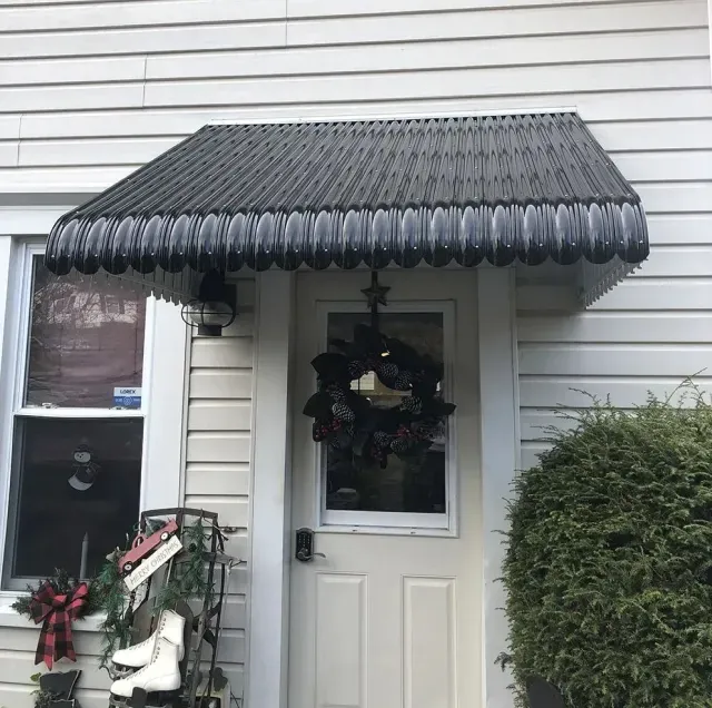 Black awning over a white front door with a wreath and a window to the left.