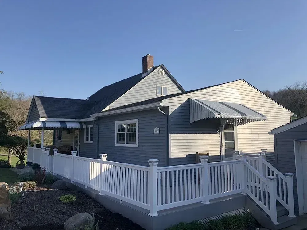 Blue-gray house with white deck and awnings, set against a clear blue sky.