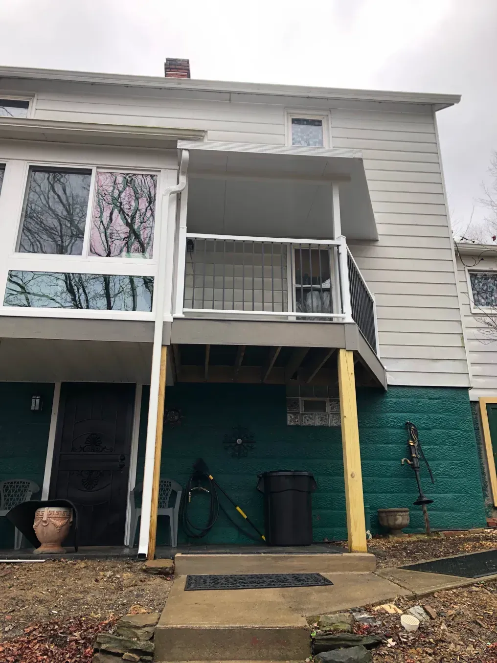 Exterior of a two-story building with a deck, green wall, and concrete walkway leading to the entrance.