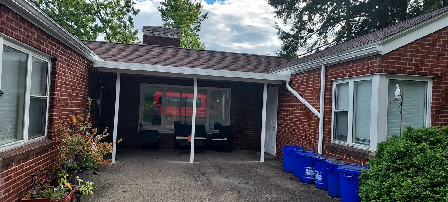 Brick house with a covered front entrance and blue trash bins.