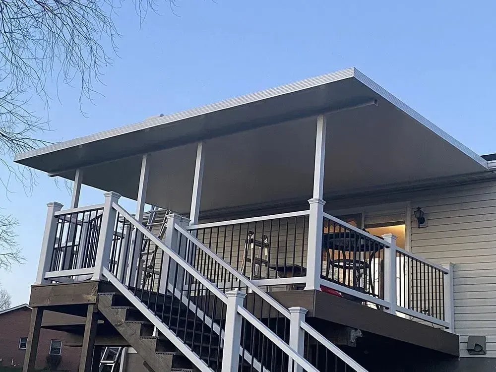 Deck with stairs, white railings, and a gray awning. House siding visible.