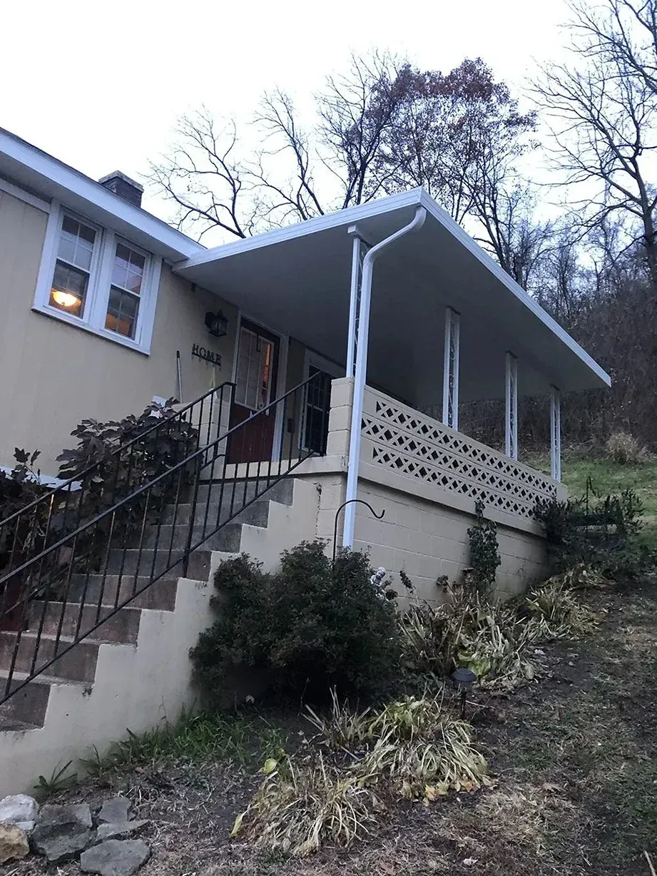 A beige house with a covered porch, concrete steps, and a sloping yard.