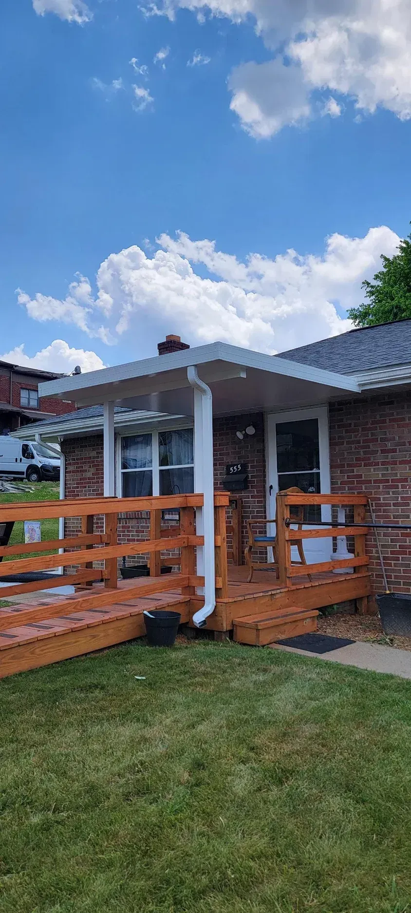 A brick house with a wooden deck and a white awning under a cloudy sky.