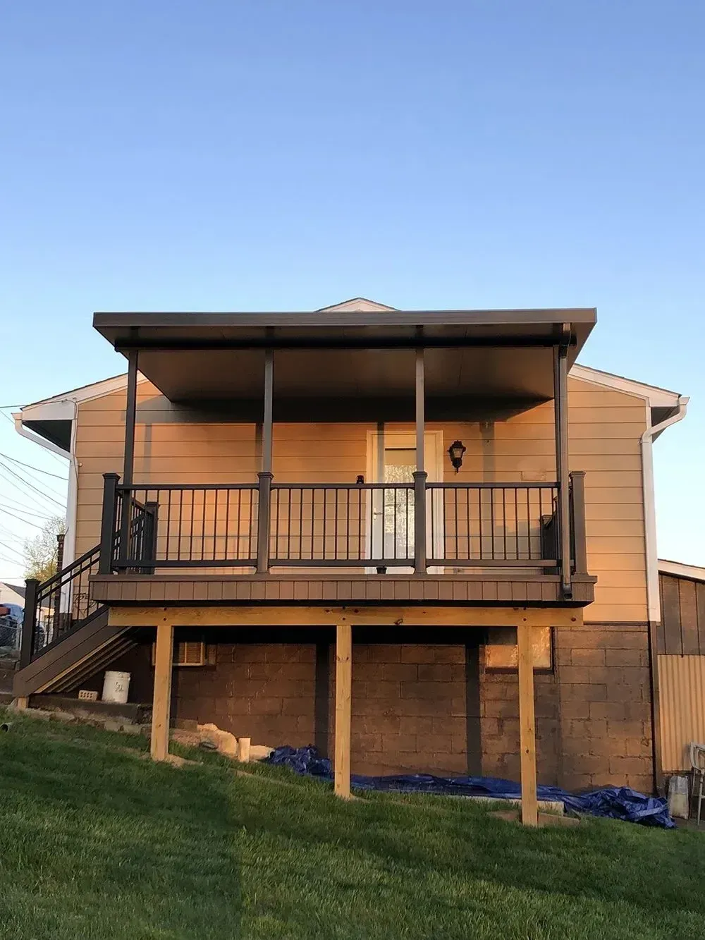 Deck with dark railing and gray roof attached to a light brown house with a door.