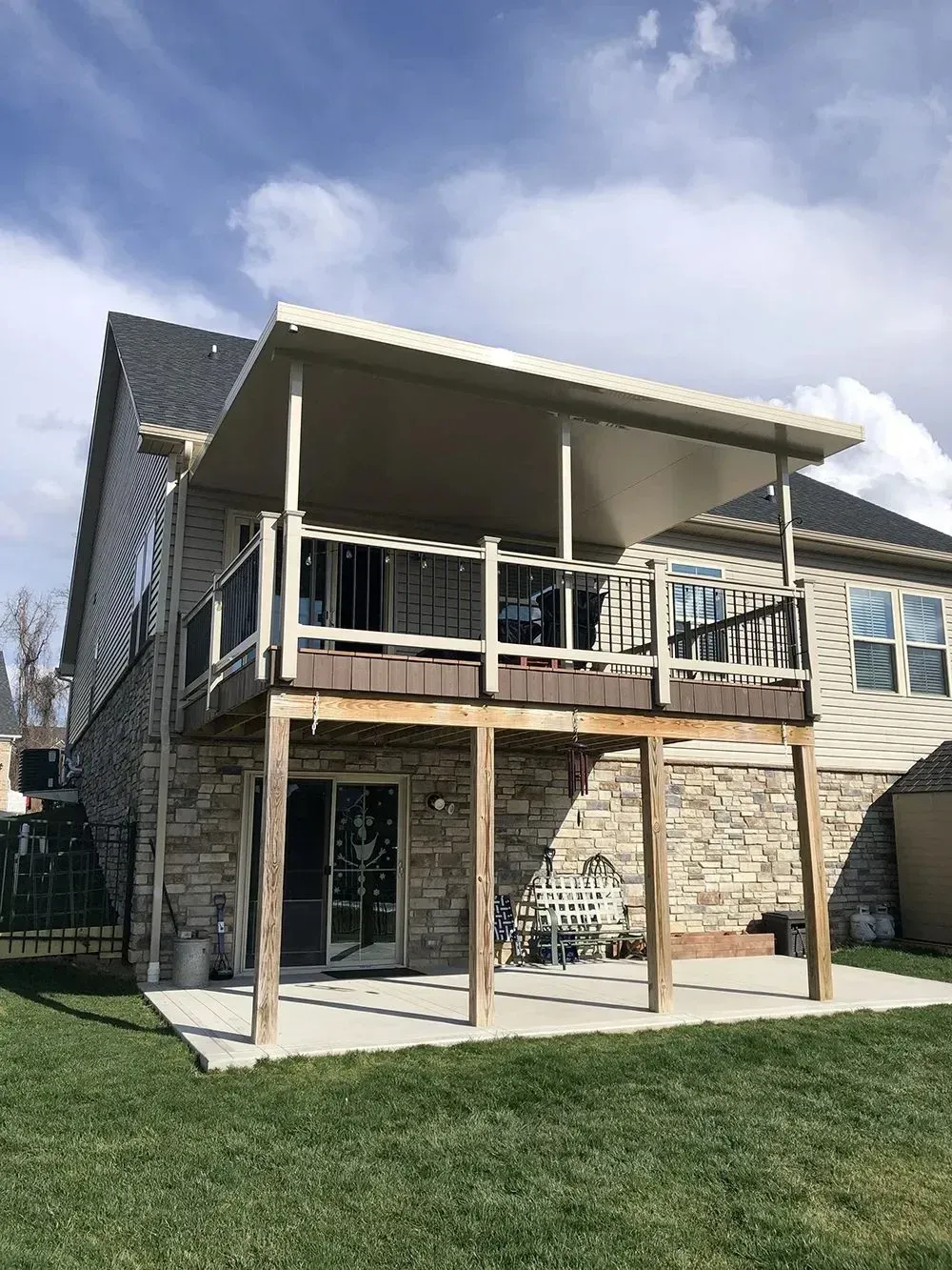 Two-story house with a wooden deck and a covered patio, featuring tan siding and stone exterior.