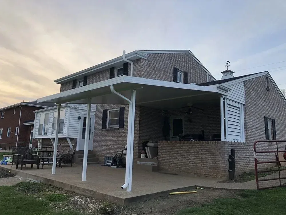 A two-story brick house with a white-framed patio cover extending from its side.