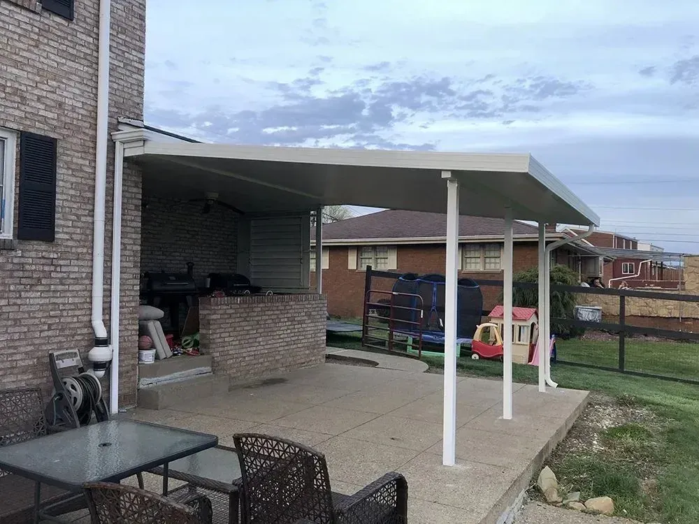 A patio with a cream-colored aluminum awning attached to a brick house. Includes furniture and yard.