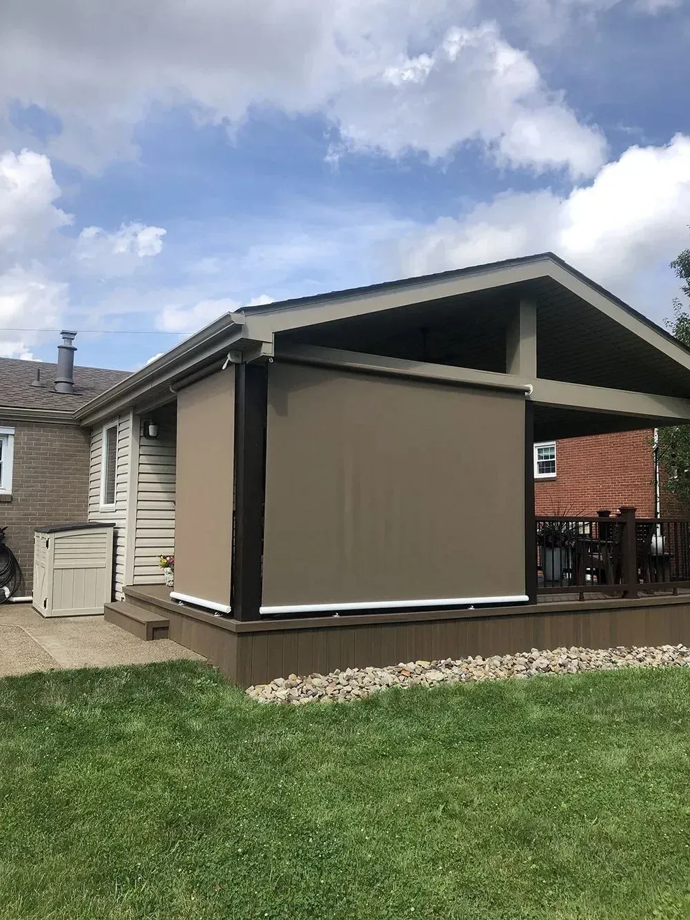 Tan outdoor shade covering a deck, with green grass and a house in the background.