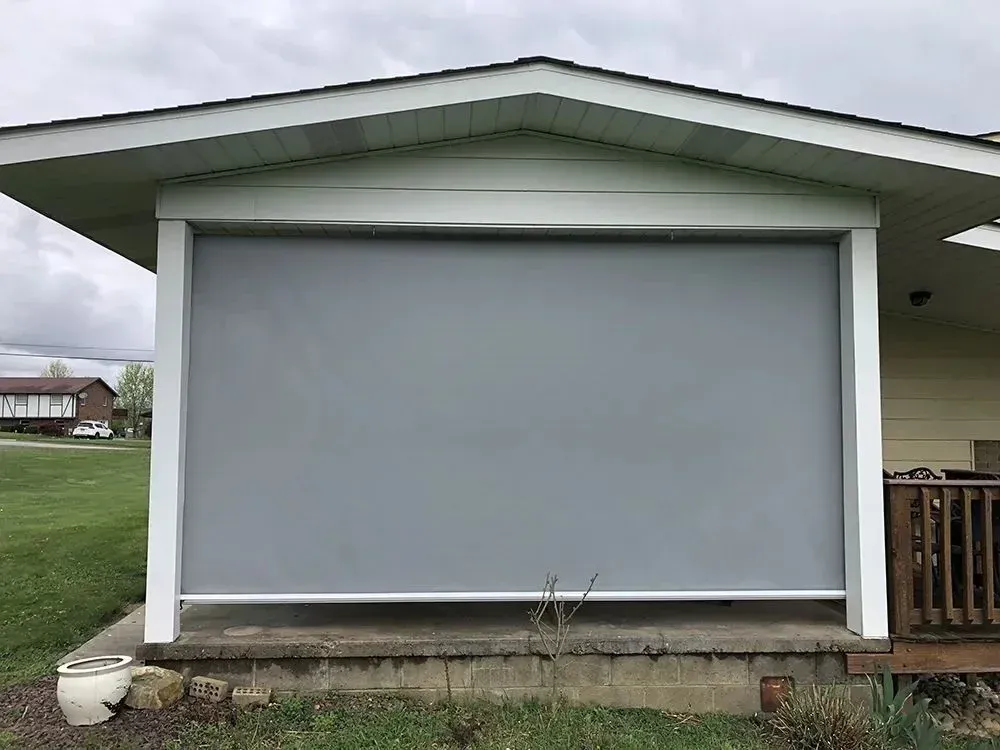 Gray outdoor screen installed on a porch. The house is white. Green grass is in the foreground.