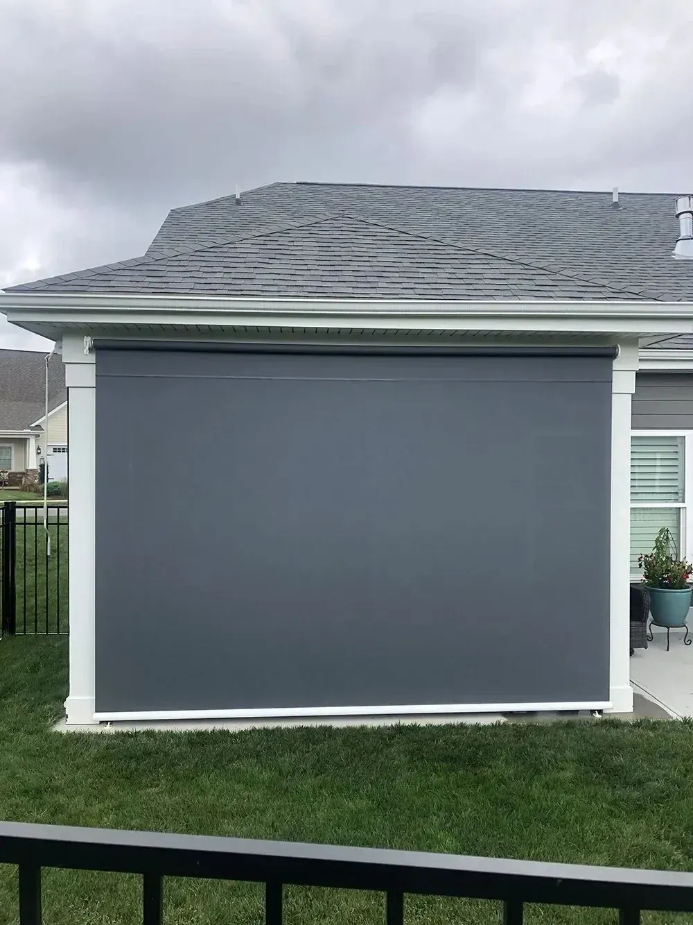 A retractable gray shade on a house's back patio, providing shade from the overcast sky.