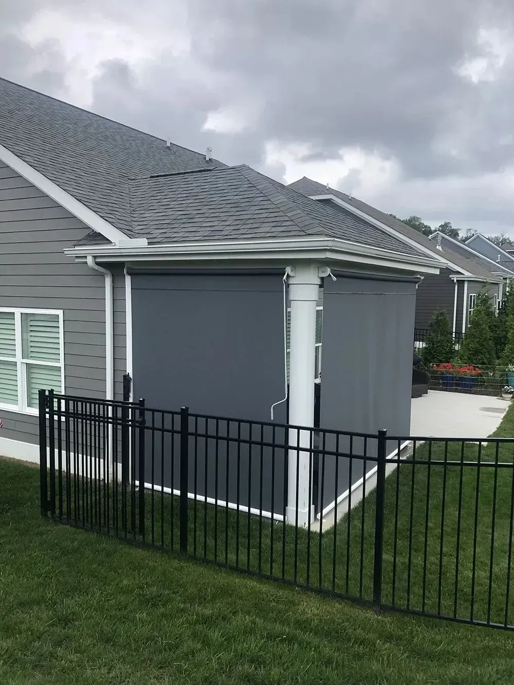 Gray patio shades on a home, behind a black fence. Overcast sky.