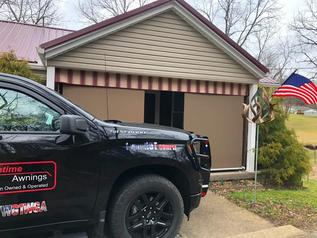 Black truck in front of a tan building with a striped awning and an American flag.