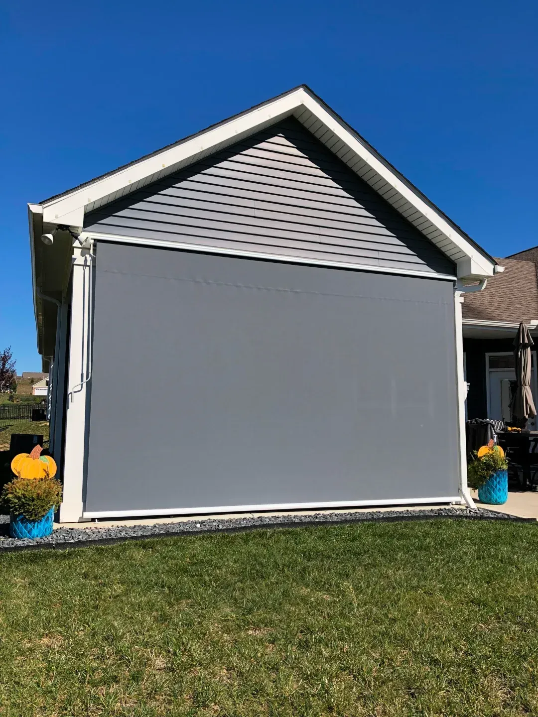 Gray outdoor shade covers a light blue-gray sided building under a clear blue sky.