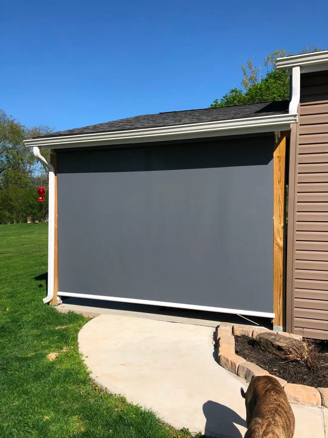 Gray retractable outdoor shade on a building with a concrete path and lawn in view.