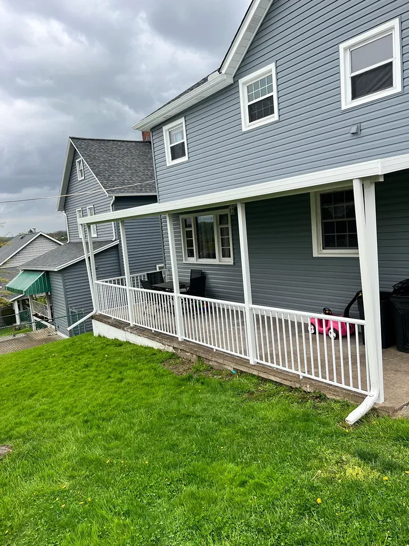 Gray house with white porch and railing, green lawn, cloudy sky.