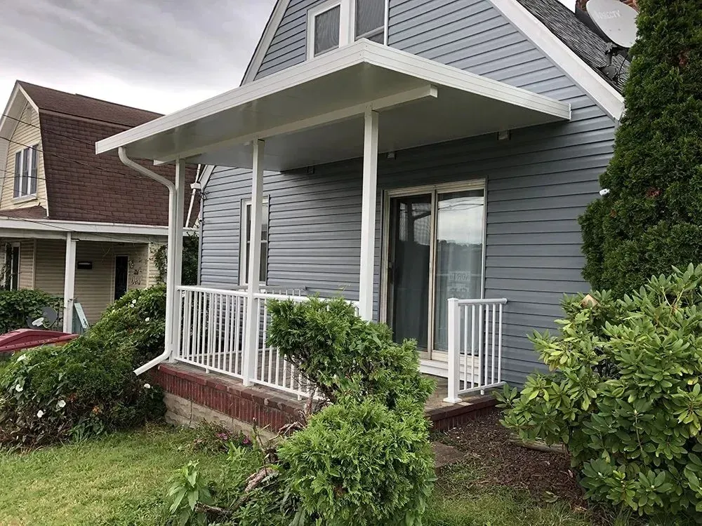 House with grey siding and white awning over a porch with white railing.