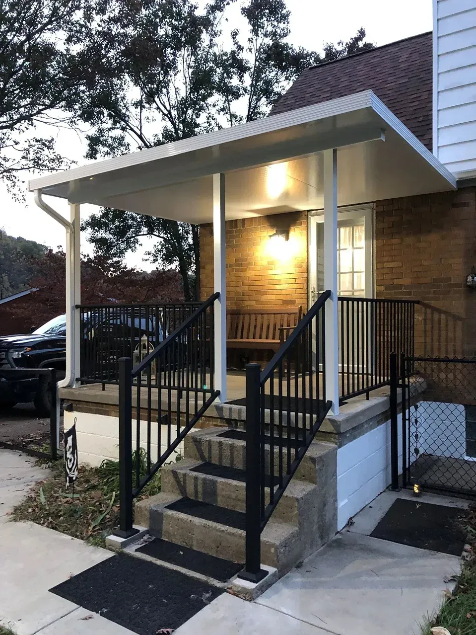A porch with steps, black railing, and a white canopy over the front door of a brick house.