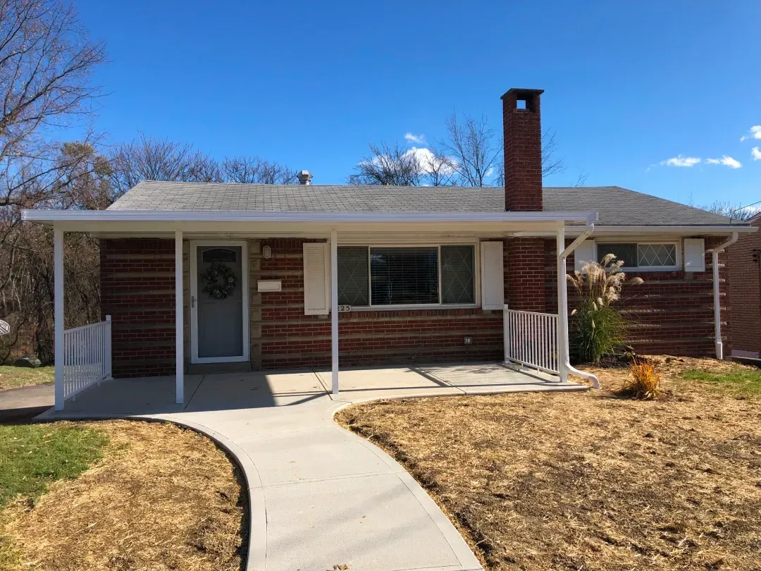 Brick ranch house with a white porch and walkway on a sunny day.