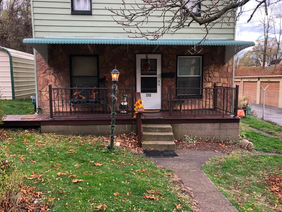 Small house with a porch. Stone facade, brown railing, and a lamppost. Icy overhang, front door, and a walkway.