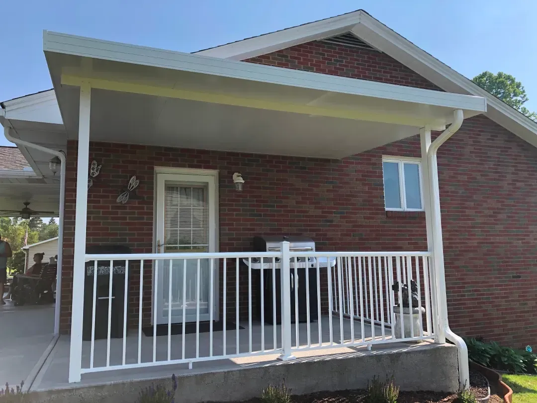 Covered patio with white railing and support beams attached to a brick house.
