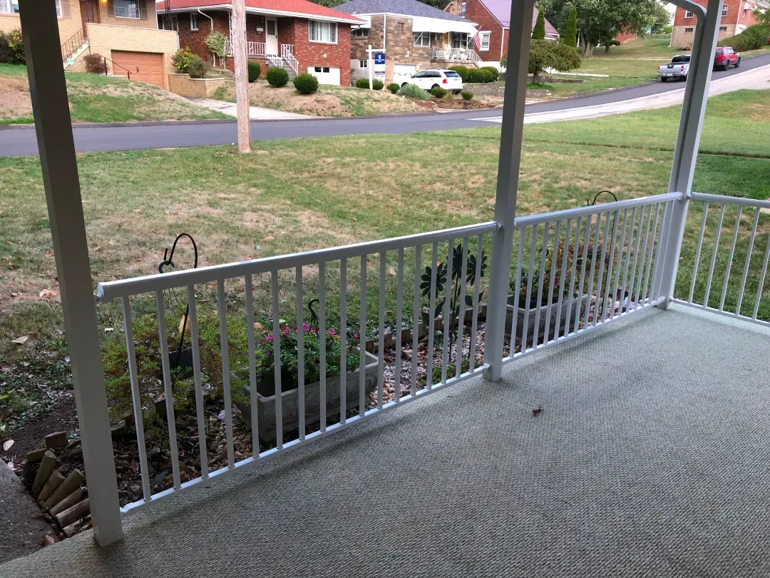 White railing on a porch overlooking a street, grass, and houses.