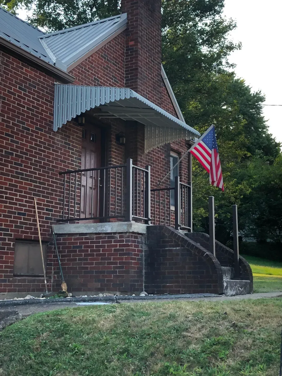 Brick house with a small porch, metal awning, and American flag.