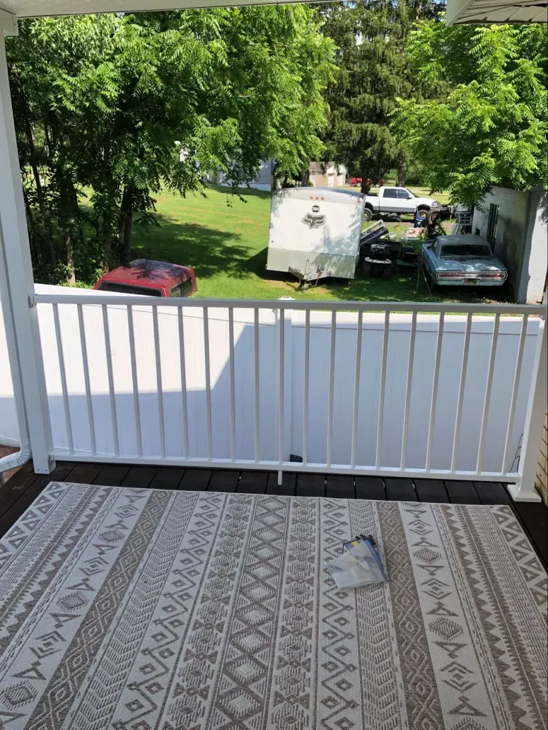 View from a deck with white railing, beige rug, and several cars in the yard.