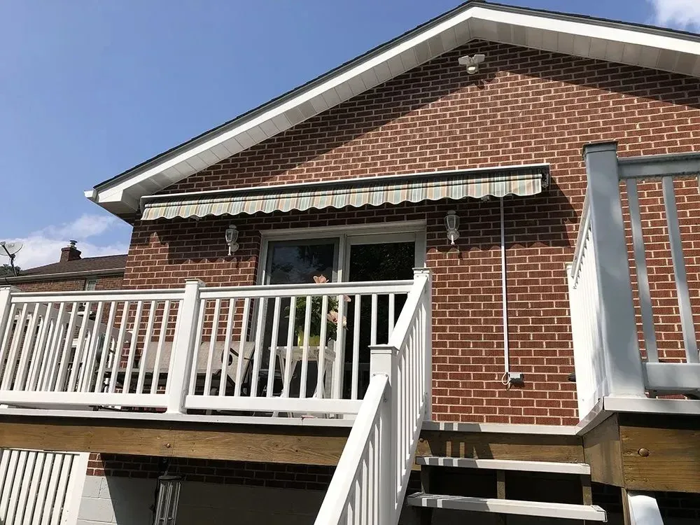 Brick house with deck, awning, and steps. White railing surrounds deck and stairs. Clear blue sky.