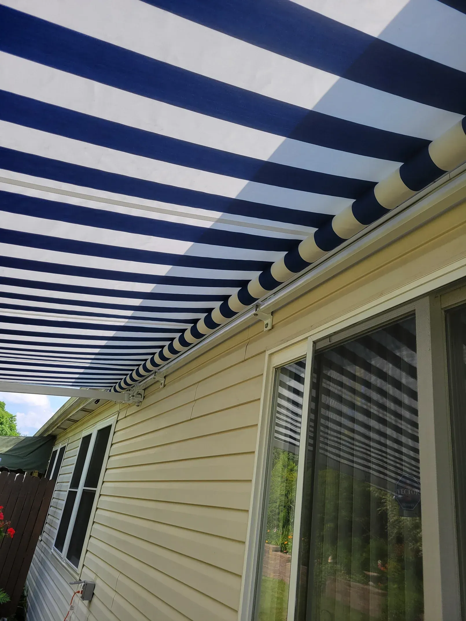Blue and white striped awning extending over a house's beige siding and windows.
