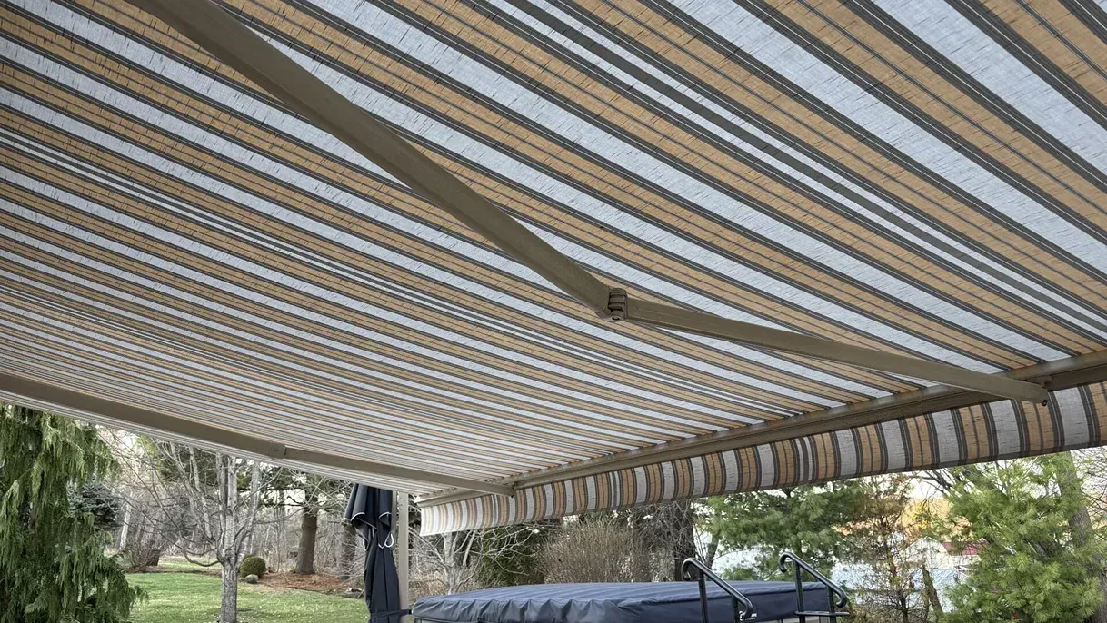 Beige and white striped retractable awning extending over an outdoor area with trees.