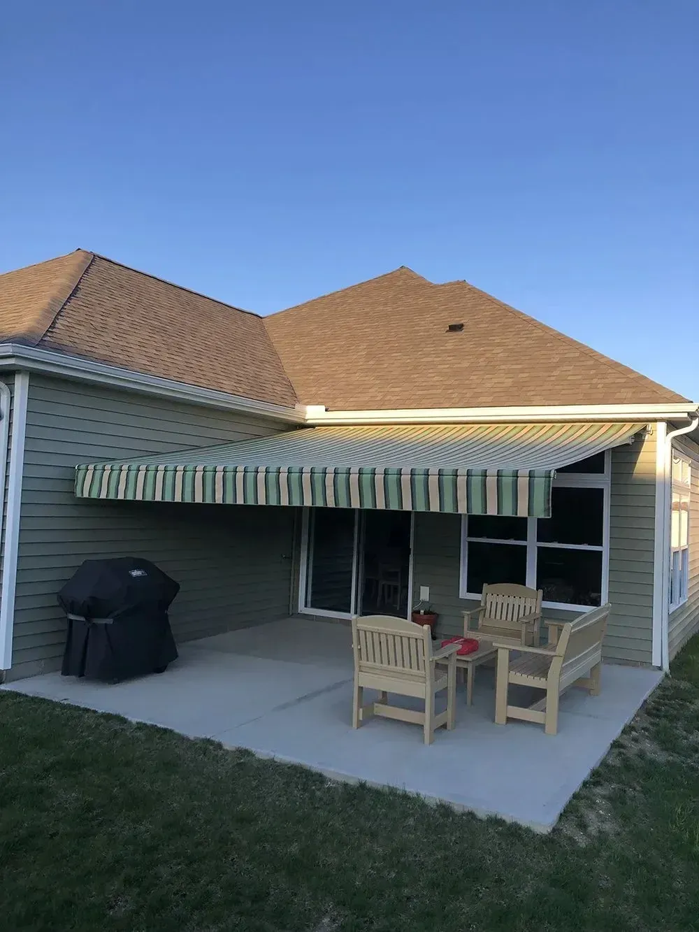 A house with a patio featuring an awning and outdoor furniture. Green and tan striped awning, light blue sky.
