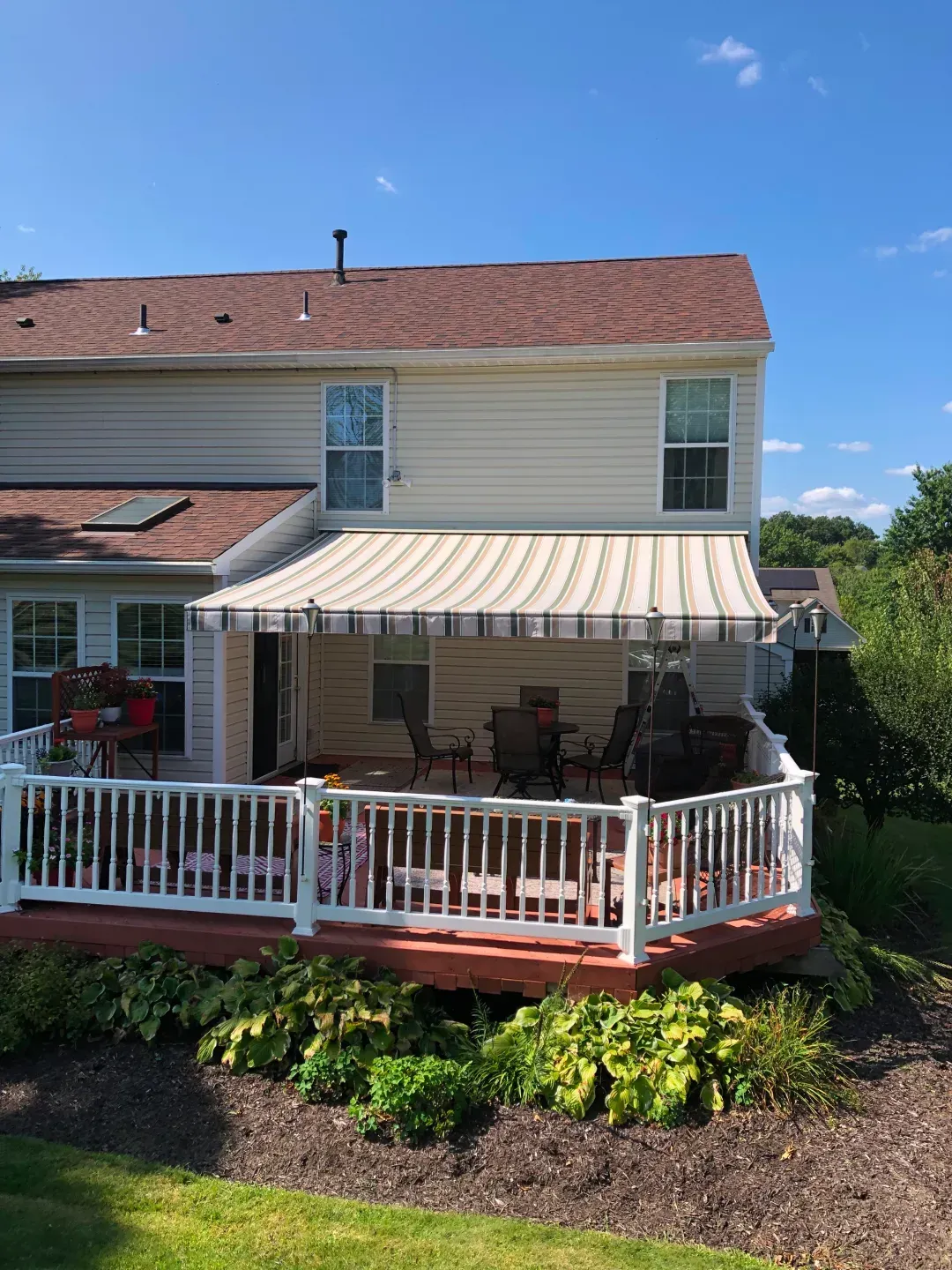 Beige house with a striped awning over a deck with furniture.